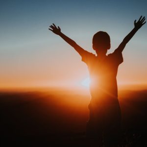 A child silhouette with raised arms enjoying a vibrant sunset, symbolizing freedom and joy.